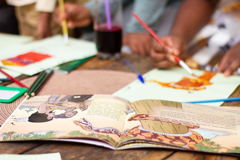 Album illustré africain ouvert sur la table, entouré de crayons et de peinture
